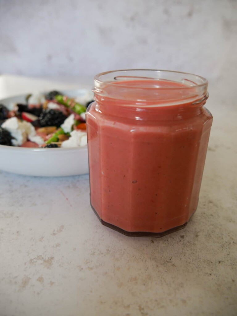 A jar of fresh raspberry vinaigrette dressing set alongside a bowl of salad.