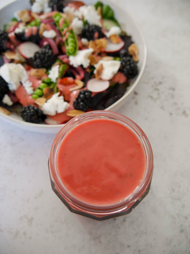 A jar of fresh raspberry vinaigrette dressing set alongside a bowl of salad.