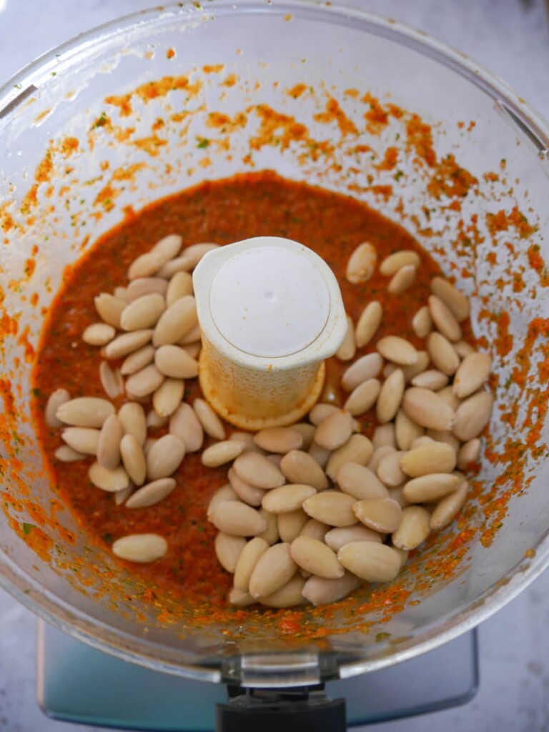 A bowl of blitzed roasted red pepper dip ingredients with added blanched almonds.