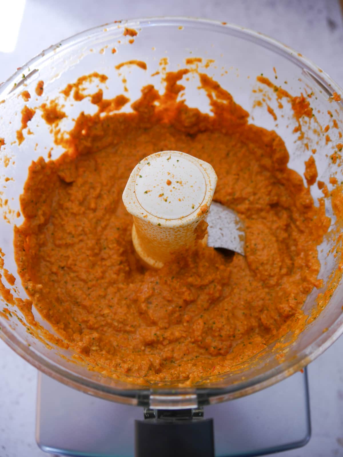 A food processor bowl filled with blitzed roasted red pepper dip.