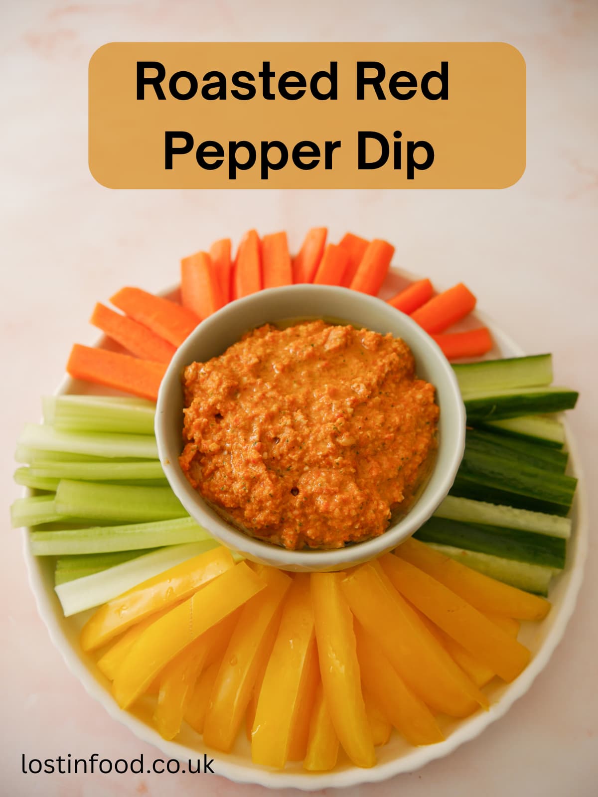 Pinnable image with recipe title and a bowl of roasted red pepper dip served with a variety of fresh vegetable sticks, including bell pepper, cucumber, celery and carrot.