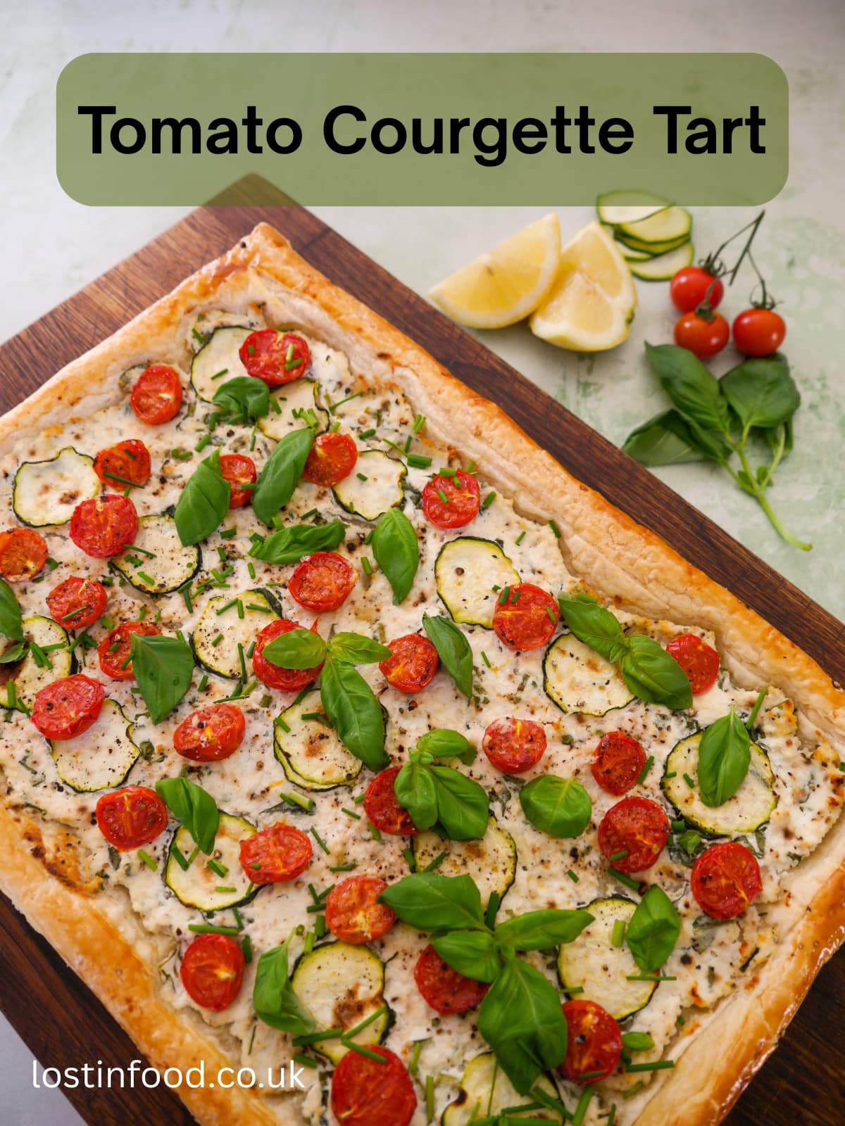 Pinnable image with recipe title and a wooden board topped with a tomato and courgette puff pastry tart, with ricotta cheese, and garnished with fresh basil and chives.