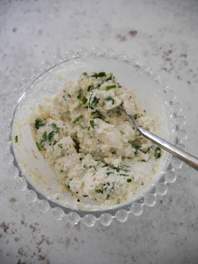A bowl of ricotta cheese, mixed with freshly chopped basil and chives.