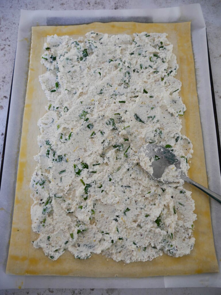 A baking sheet topped with a sheet of puff pastry, topped with a ricotta cheese and herb mixture.