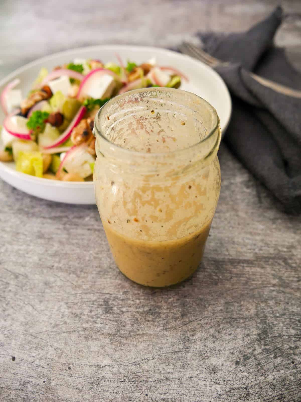 A jar of apple cider vinaigrette dressing with vegetable salad set alongside.