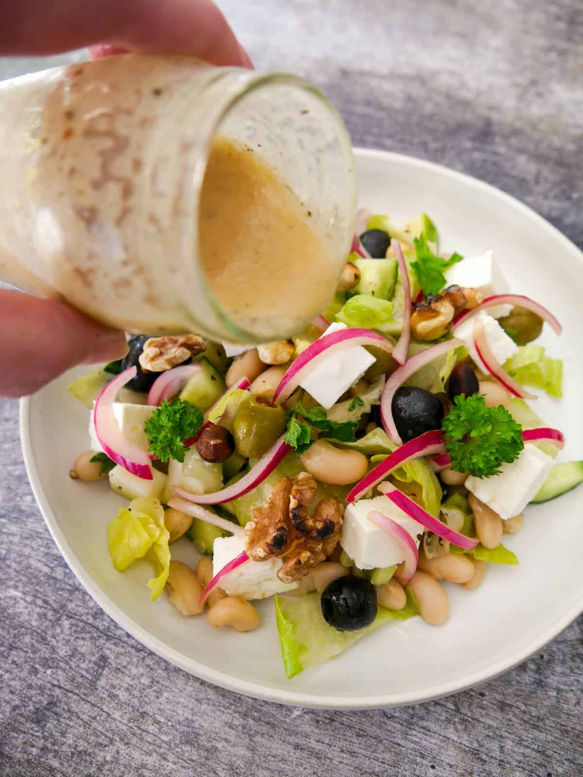 Apple cider vinaigrette dressing being poured over a white bean and vegetable salad.