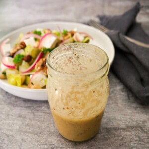 A jar of apple cider vinaigrette dressing with vegetable salad set alongside.