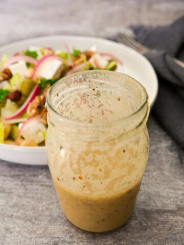 A jar of apple cider vinaigrette dressing with vegetable salad set alongside.