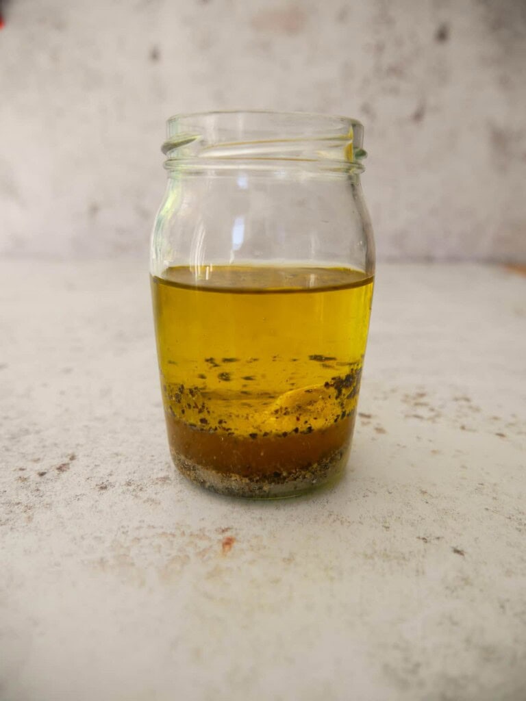 A jar with the ingredients for apple cider vinaigrette layered up.