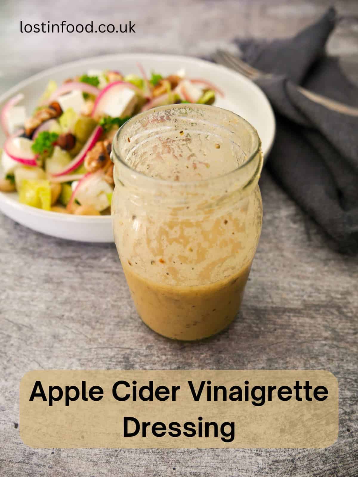 Pinnable image with recipe title and a jar of apple cider vinaigrette dressing, with a salad set alongside.