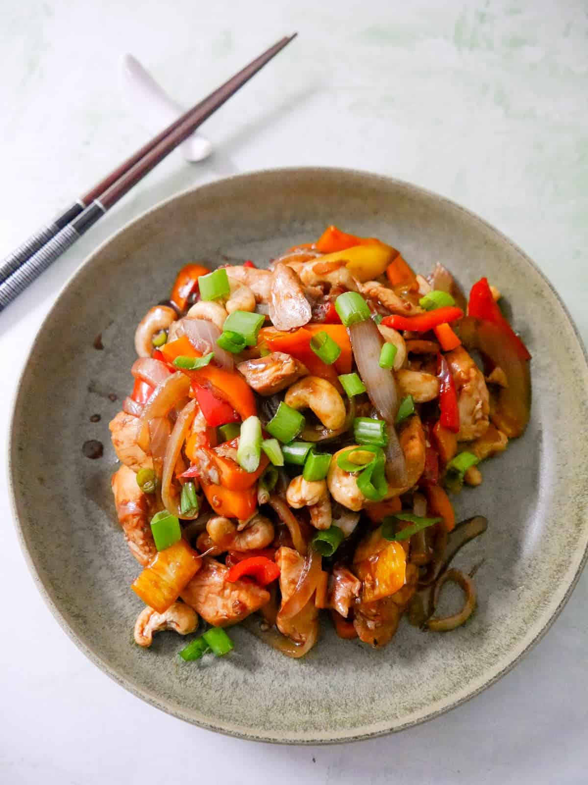 A bowl of stir-fried chicken and cashew nuts, with chopsticks set alongside.