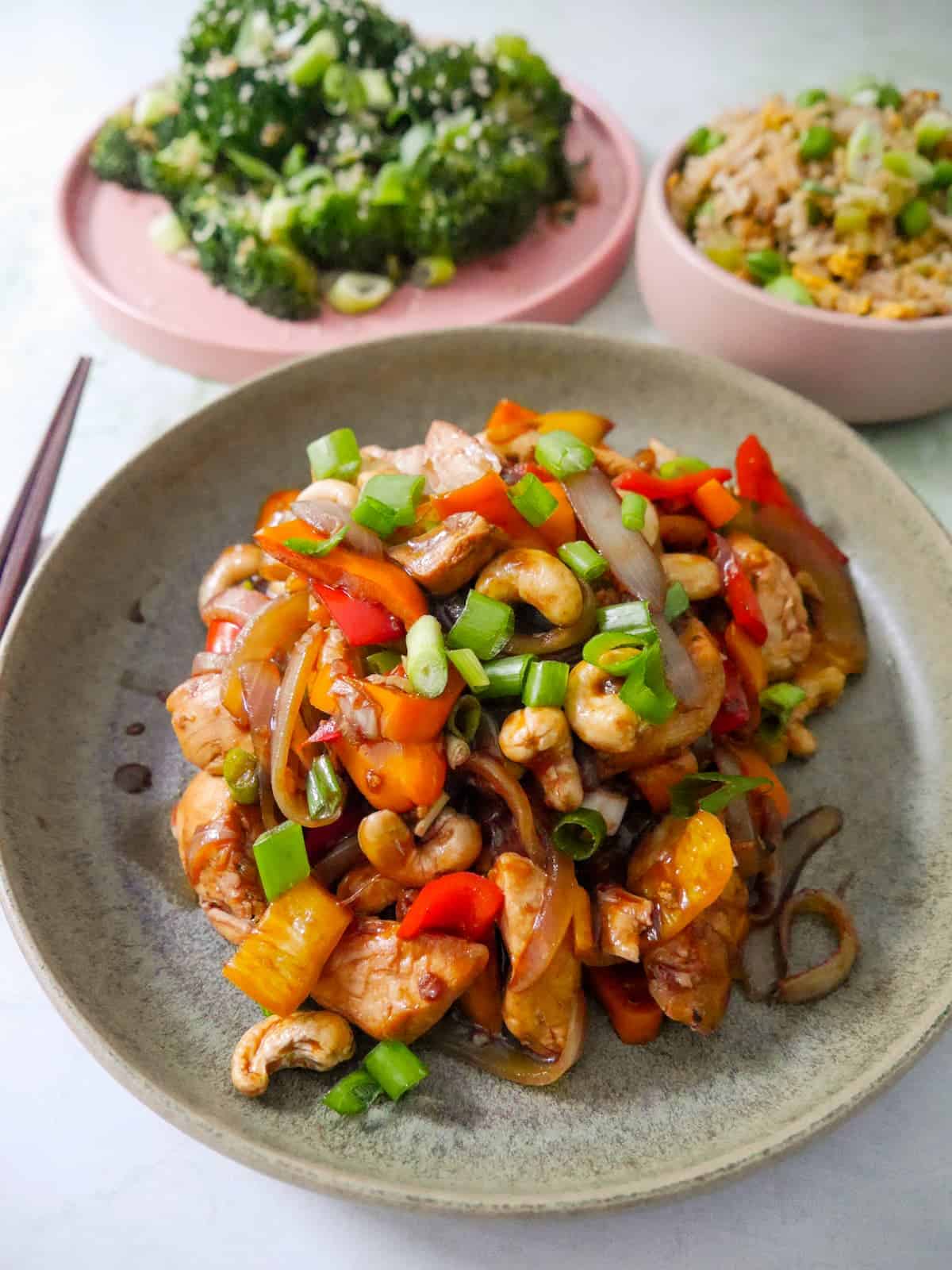 A bowl of stir-fried chicken and cashew nuts, with bowls of egg fried rice and stir-fried broccoli set alongside.