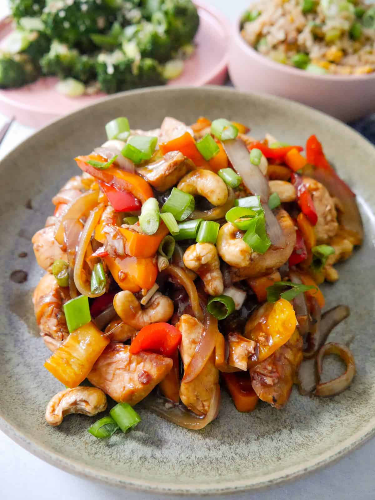 A bowl of stir-fried chicken and cashew nuts, with bowls of egg fried rice and stir-fried broccoli set alongside.