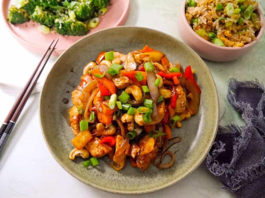 A bowl of stir-fried chicken and cashew nuts, with bowls of egg fried rice and stir-fried broccoli set alongside.