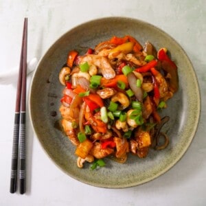 A bowl of stir-fried chicken and cashew nuts, with chopsticks set alongside.