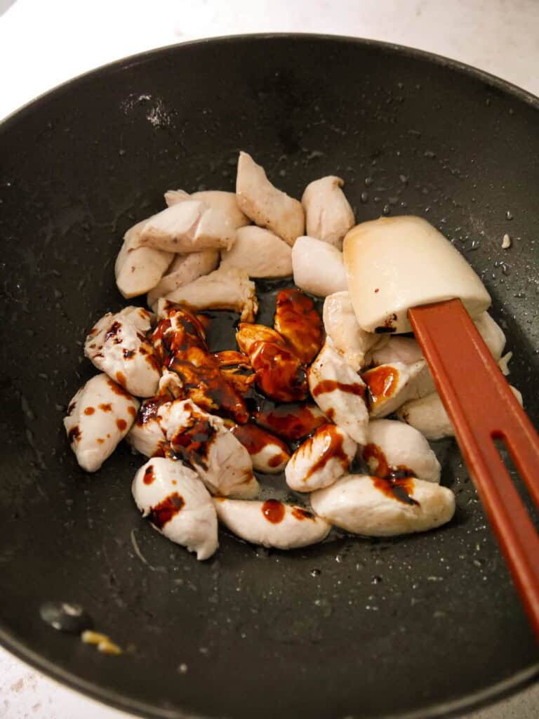 A wok of stir-fried chicken with added soy sauce.