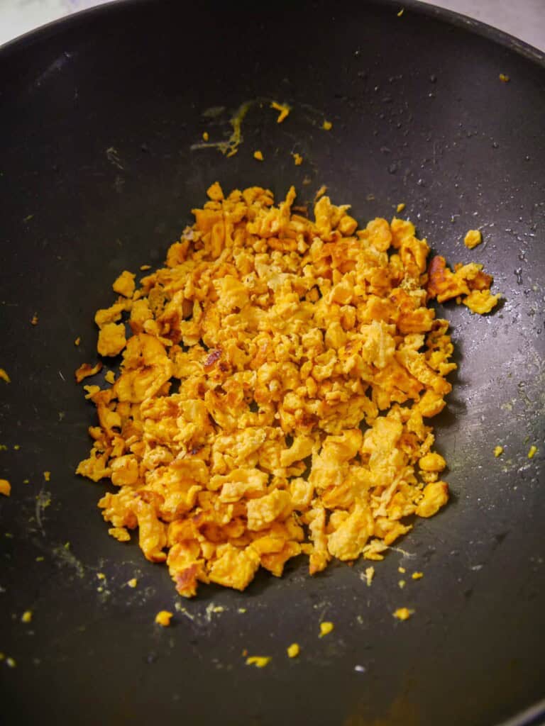 A wok of stir-fried egg, broken up into small pieces with a spatula.