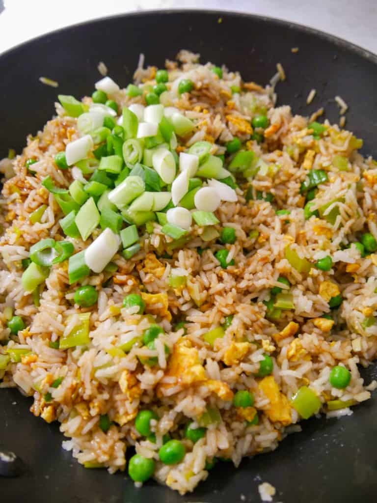 A wok of egg fried rice with sliced fresh spring onions being added.