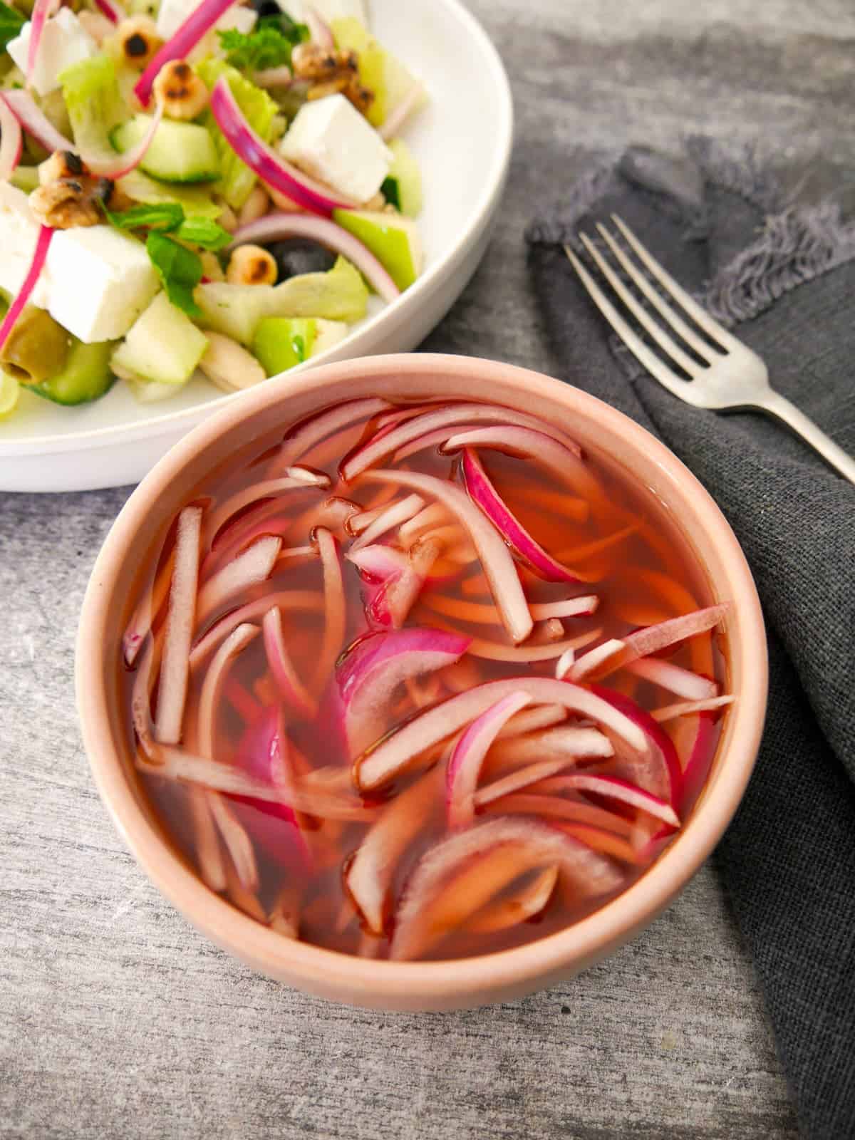 A bowl of quick pickled red onion, with a salad set alongside.