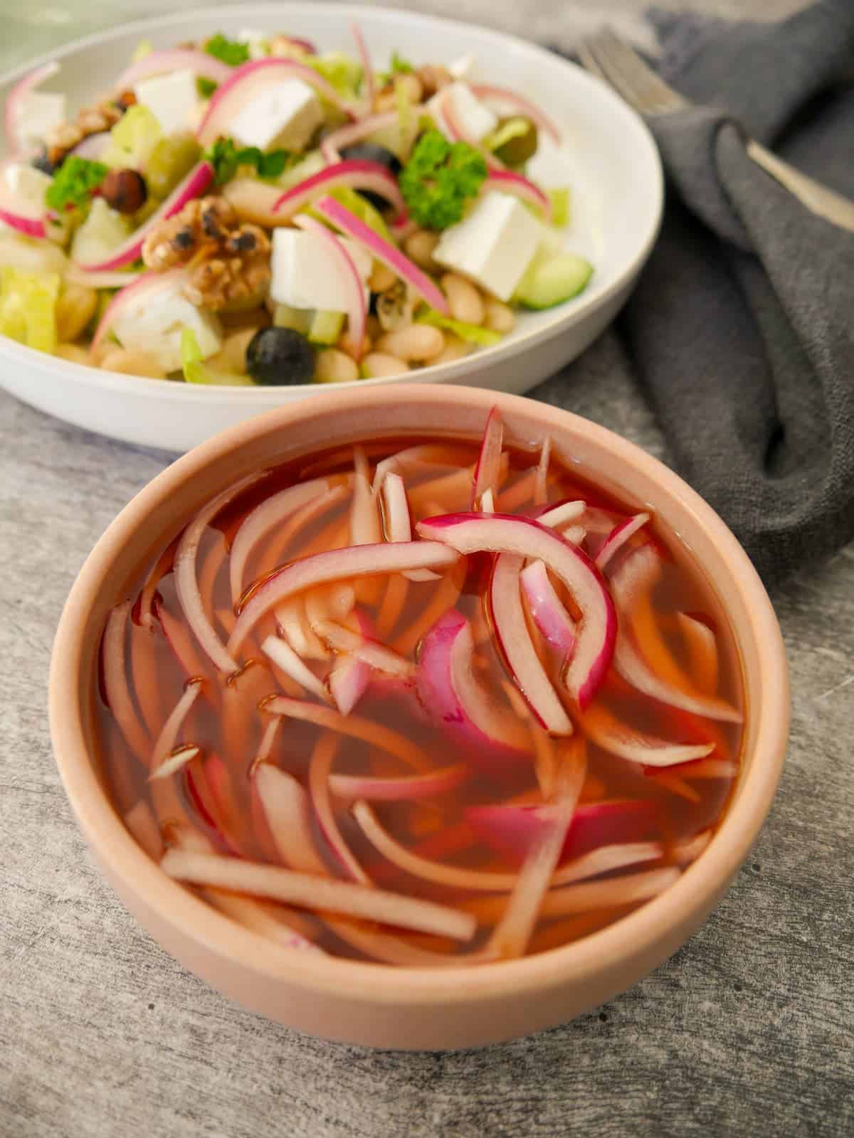 A bowl of quick pickled red onion, with a salad set alongside.