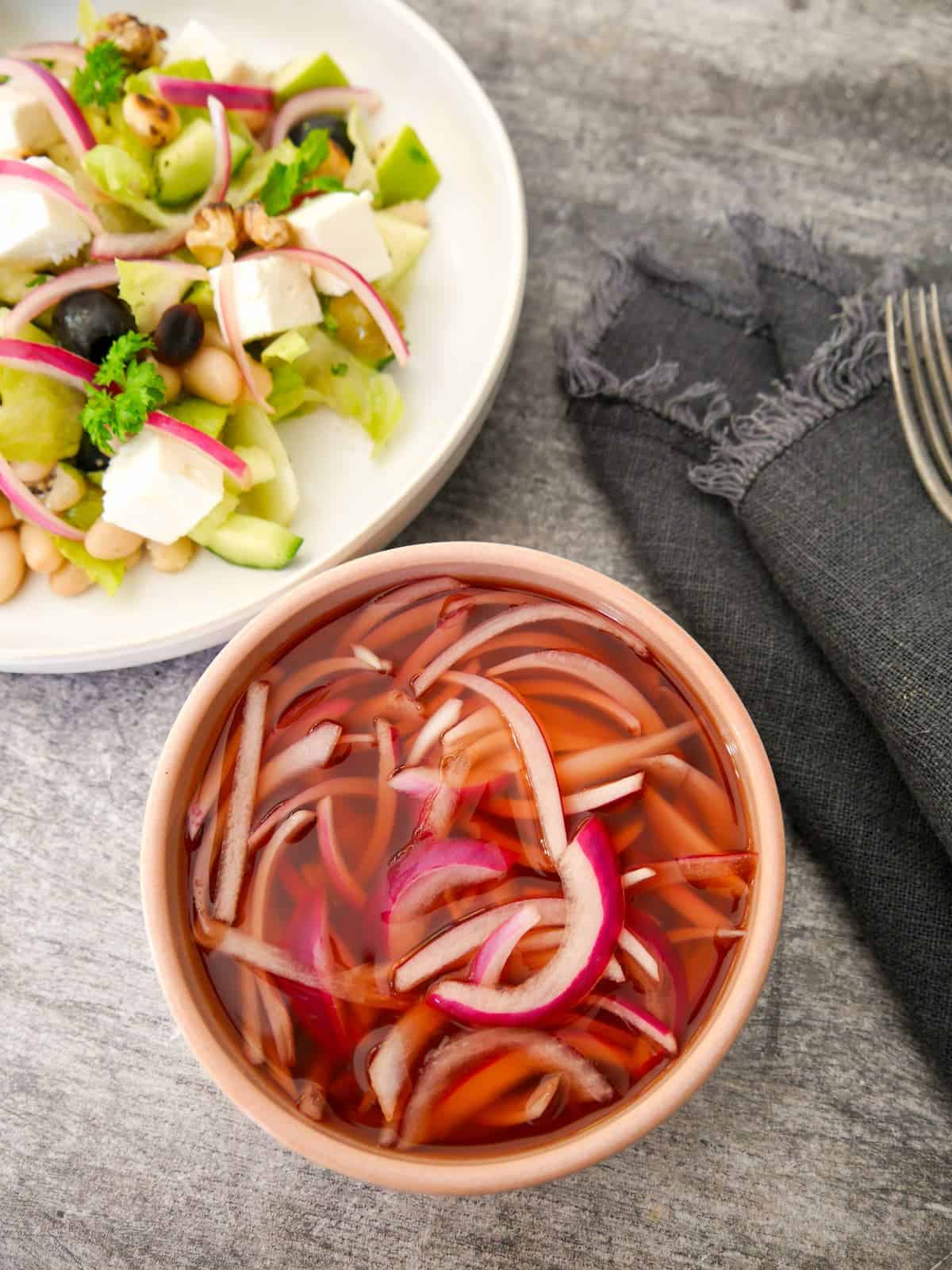 A bowl of quick pickled red onion, with a salad set alongside.