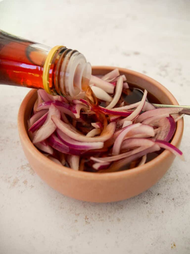 A bowl of pickled red onions, being topped up with red wine vinegar, until the onions are covered.