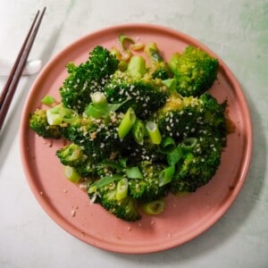 A plate of stir-fried broccoli garnished with sesame seeds and sliced spring onions.