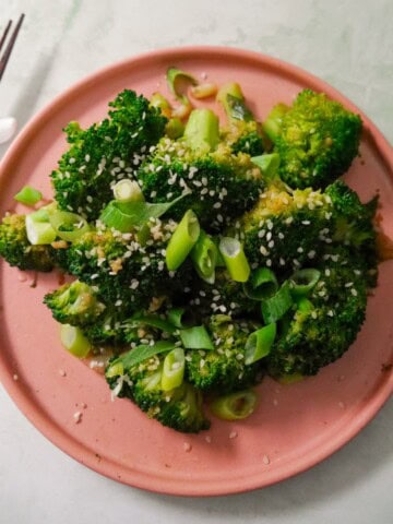 A plate of stir-fried broccoli garnished with sesame seeds and sliced spring onions.