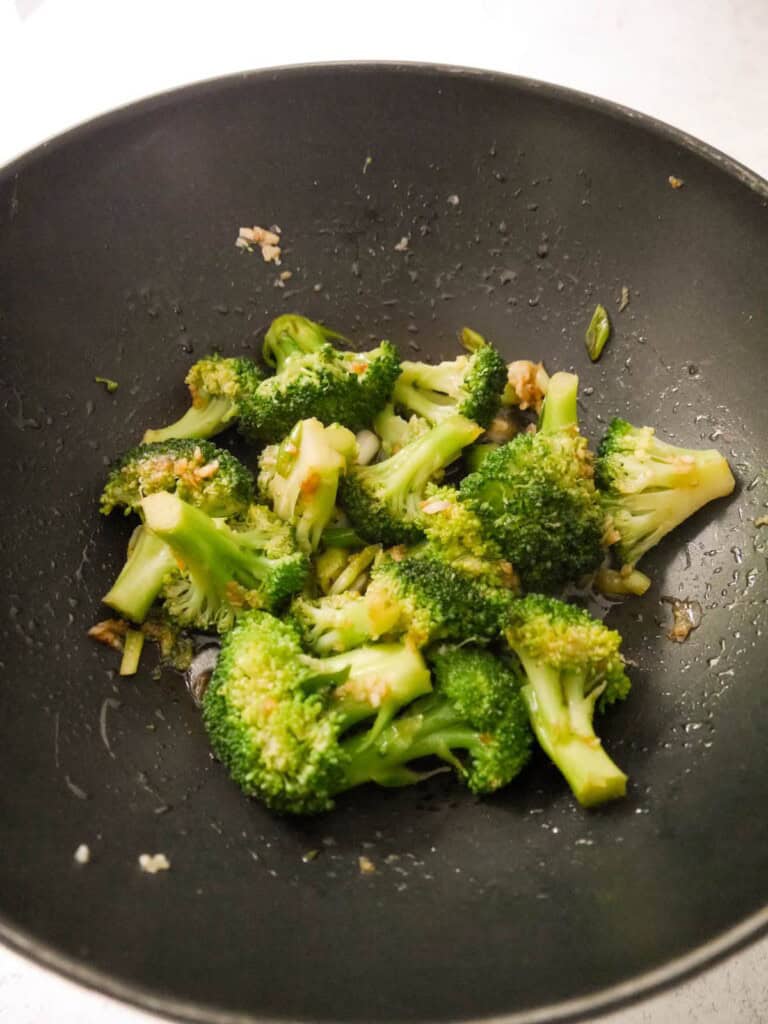 A wok with stir-fried broccoli, garlic and spring onions.