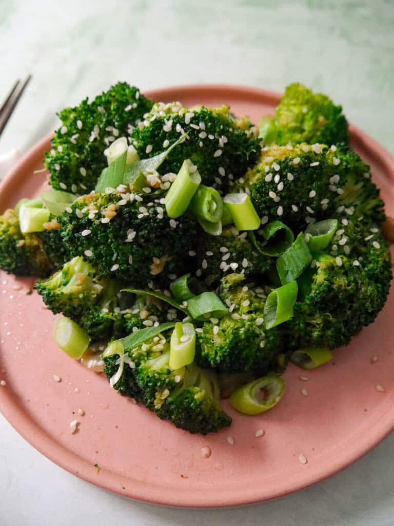 A plate of stir-fried broccoli garnished with sesame seeds and sliced spring onions.