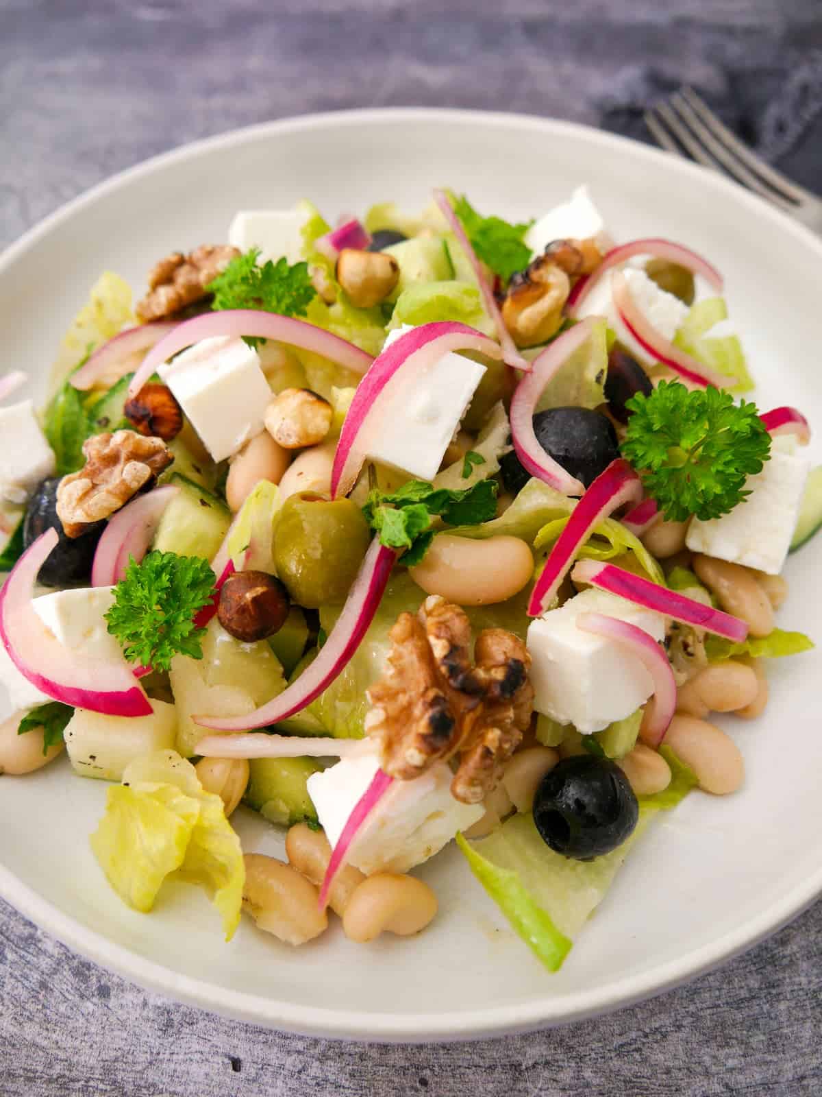 A bowl of white bean and feta salad, which olives, pickled red onions and toasted nuts.