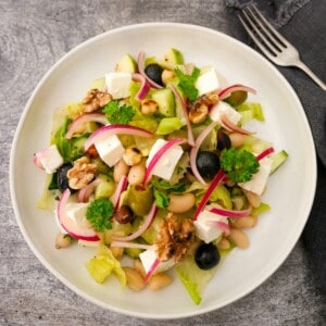 A bowl of white bean and feta salad, which olives, pickled red onions and toasted nuts.