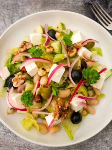 A bowl of white bean and feta salad, which olives, pickled red onions and toasted nuts.