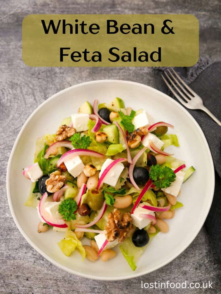 Pinnable image with recipe title and a bowl of white bean and feta salad, which olives, pickled red onions and toasted nuts.