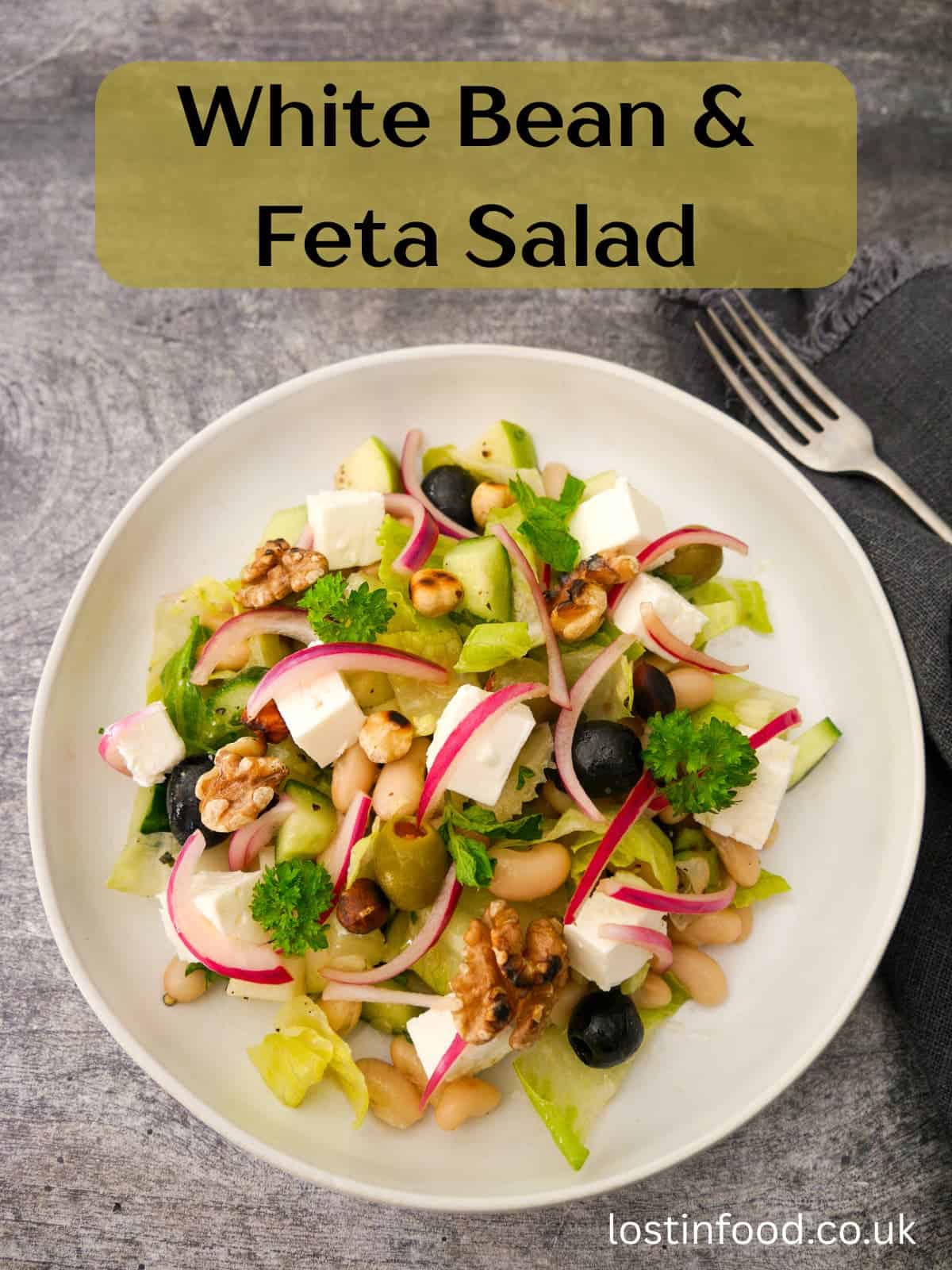 Pinnable image with recipe title and a bowl of white bean and feta salad, which olives, pickled red onions and toasted nuts.