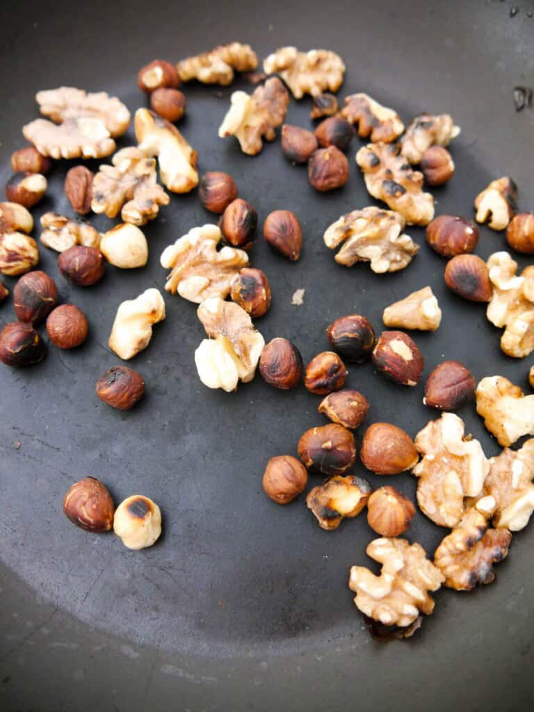 Walnuts and hazelnuts being dry roasted in a non stick frying pan.