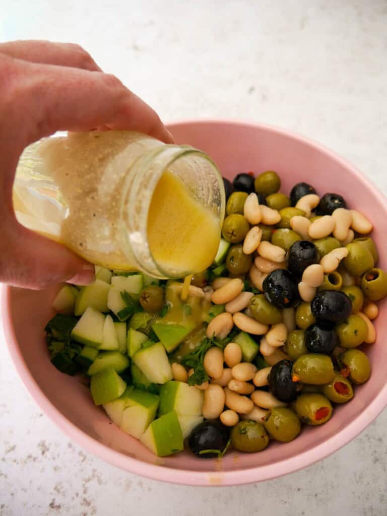 A bowl of salad ingredients with apple cider vinaigrette dressing being poured over.