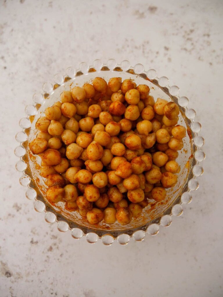 A bowl of canned chickpeas coated in olive oil and dry spices.