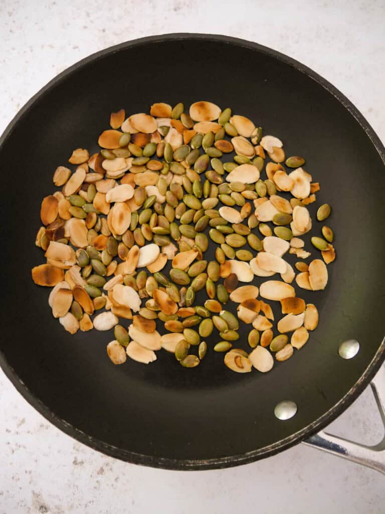 A dry non-stick frying pan with toasted flaked almonds and pumpkin seeds.