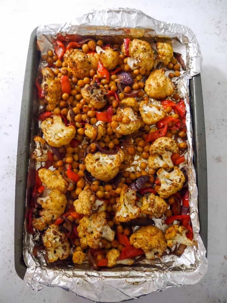 A foil lined baking sheet with roasted cauliflower florets, sliced red onion, red pepper and chickpeas.
