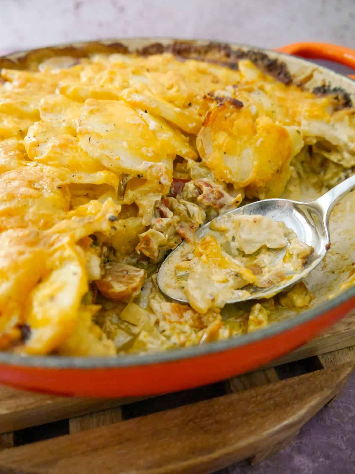 A cast iron skillet filled with chicken and bacon bake in a cider sauce, with a serving removed and serving spoon.