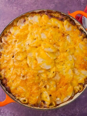 A cast iron skillet filled with chicken and bacon bake in a cider sauce.