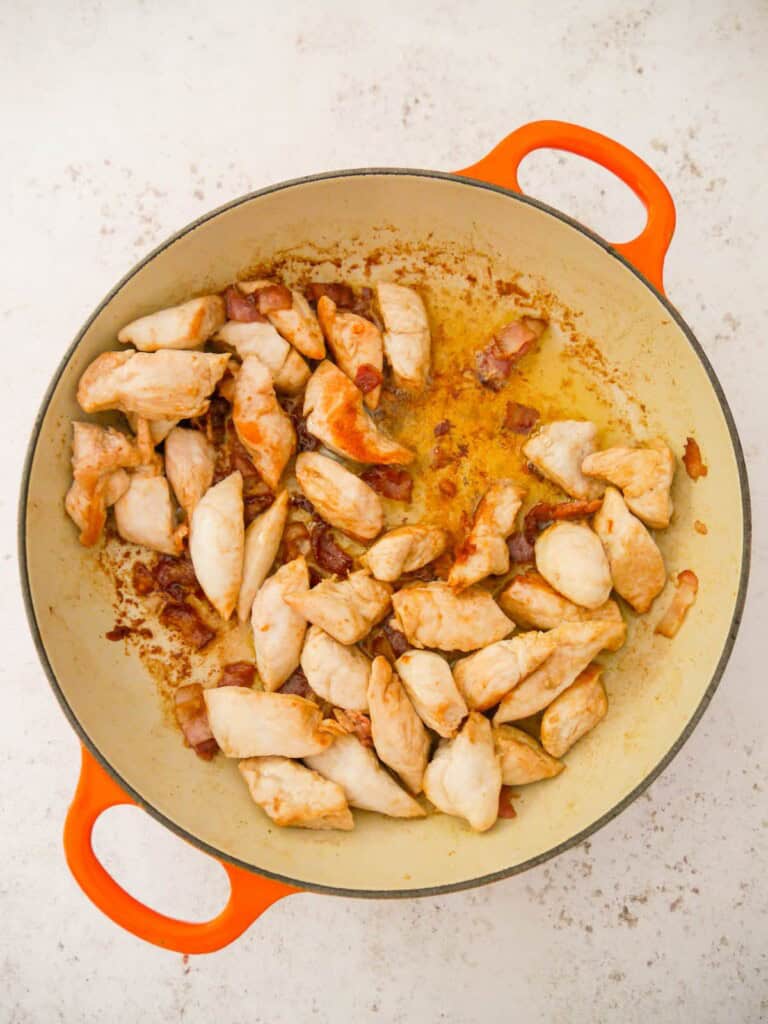 A cast iron skillet filled with sauteed chicken breast pieces and bacon.