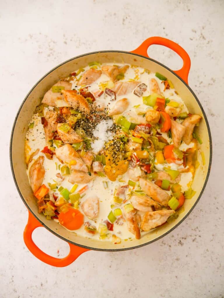 A cast iron skillet filled with sauteed chicken, bacon and vegetables, with double cream, mustard and seasoning added.