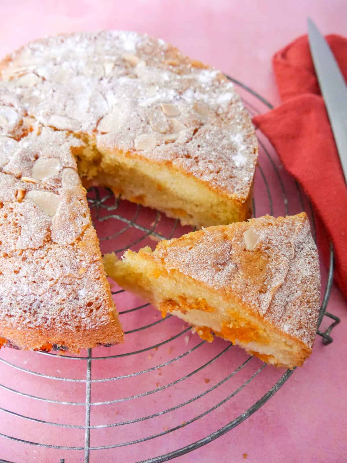 Fresh apricot cake set on a wire cooling rack with a slice cut from the cake.