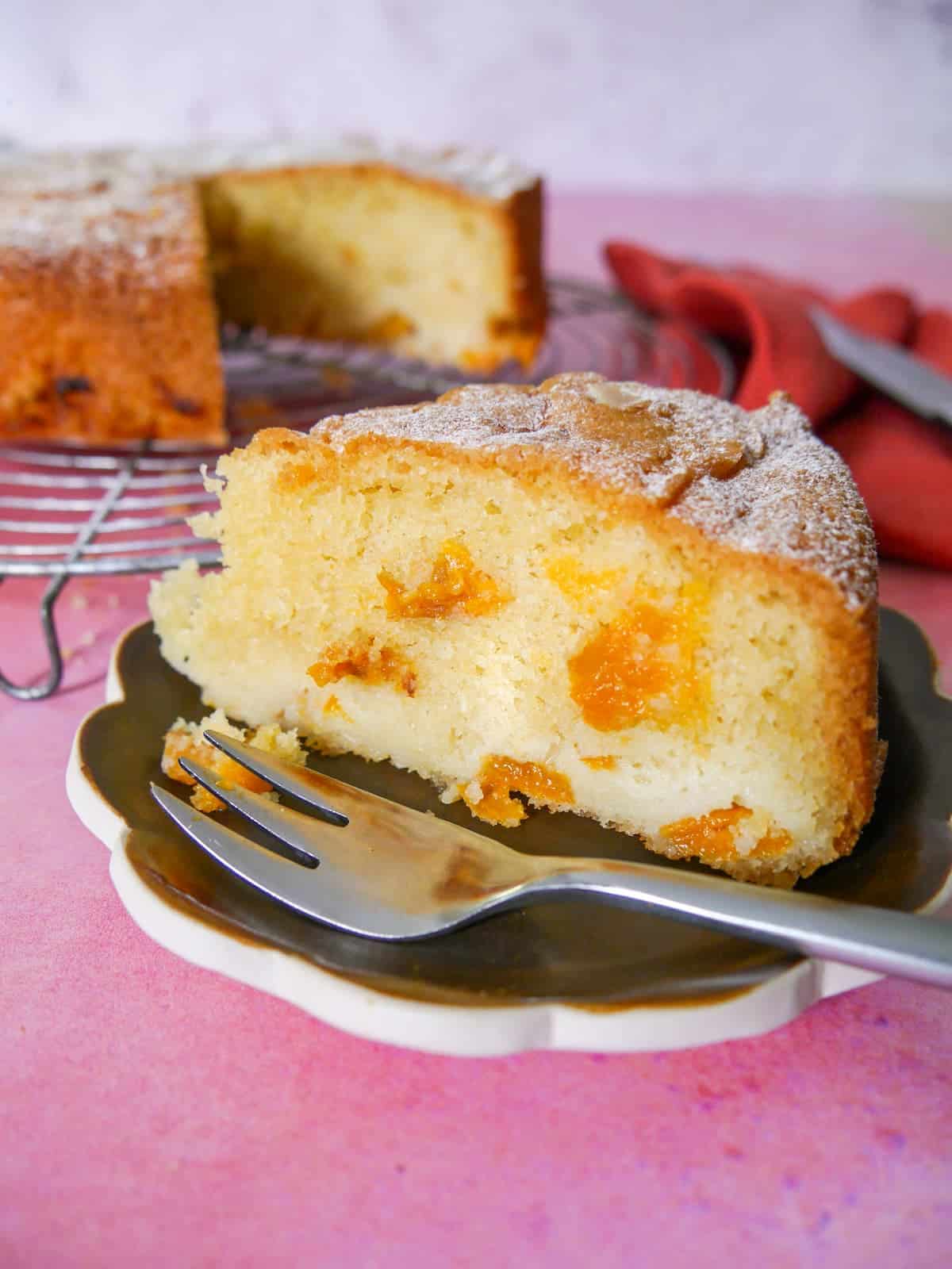 Fresh apricot cake set on a wire cooling rack with a slice cut from the cake and set on a small plate with a fork.