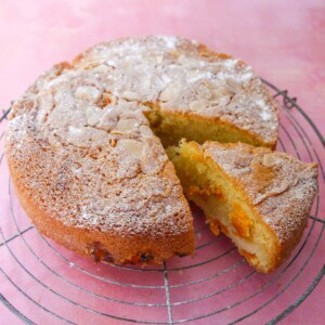 Fresh apricot cake set on a wire cooling rack with a slice cut from the cake.