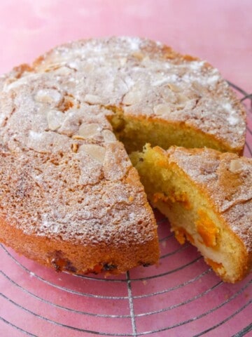 Fresh apricot cake set on a wire cooling rack with a slice cut from the cake.