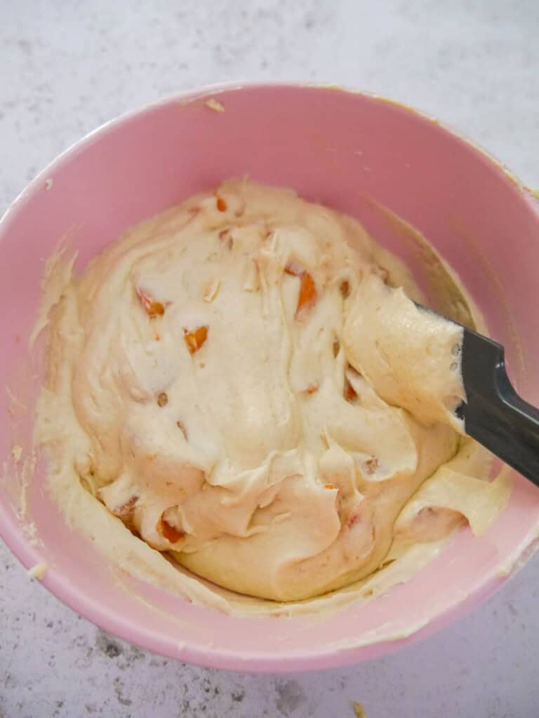 A pink bowl where the chopped fresh apricots are being stirred through the raw cake mixture.