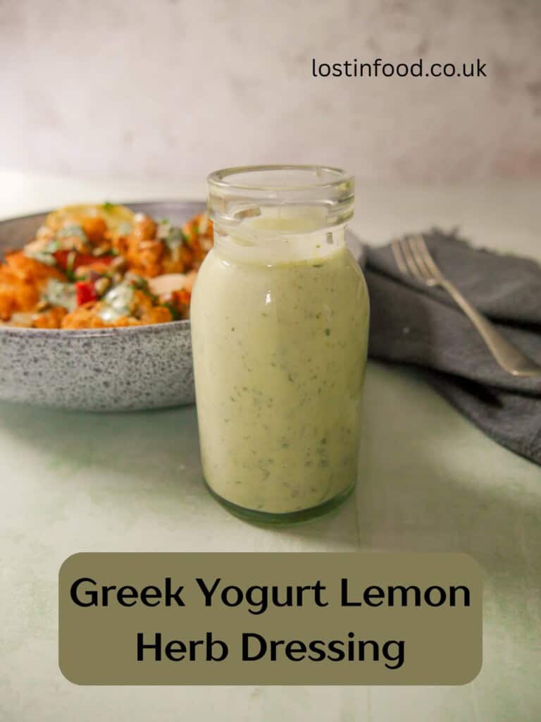 Pinnable image and recipe title with an image of a jar of Greek yogurt lemon herb dressing with a bowl of roasted cauliflower and chickpeas set alongside.
